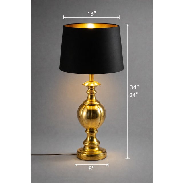 An elegant Hollywood Regency brass urn table lamp featuring its striking original black drum shade with luminous gold...