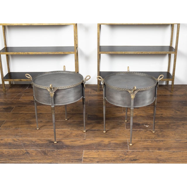 A pair of Trouvailles metal and brass round top side tables from the mid-20th century with two doors, swan necks and wing...