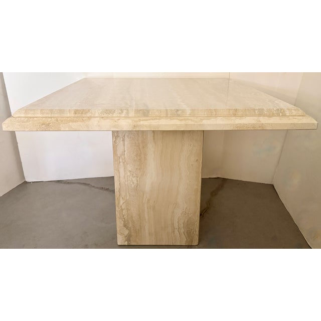 Modernist Italian game table made of beige travertine. Solid stone top and a separate square pedestal base, with a smooth,...