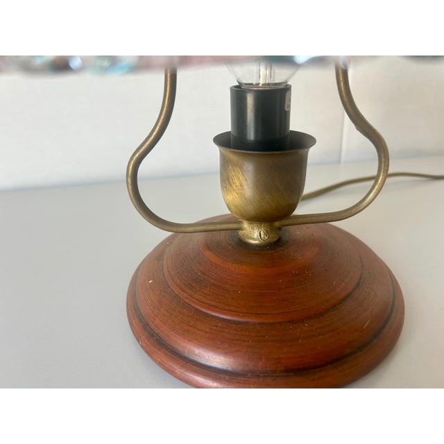 The table lamp has a cherry wood base and a brass arch. The glass diffuser is available in amethyst and aqua green....