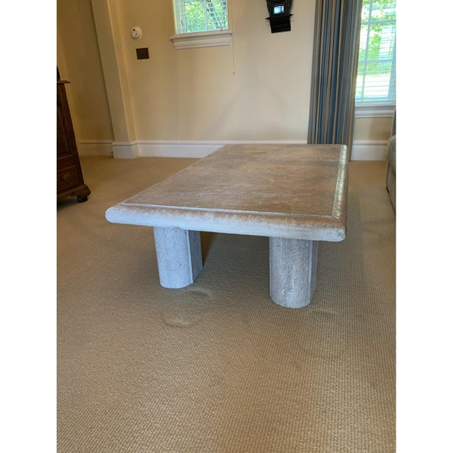 A large and heavy rectangular travertine stone coffee table with a beveled edge, four stout cylindrical legs and a chunky,...