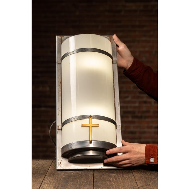 A striking ecclesiastical wall sconce built around a tall cylindrical opaline glass shade framed in steel bands and...