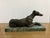 This product is an antique or vintage bronze sculpture of a greyhound dog lying down on a marble base. The figurine...