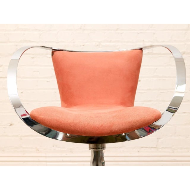 glamorous 1970s swivel armchair with a sculptural chrome halo frame and soft blush velvet upholstery. The continuous...