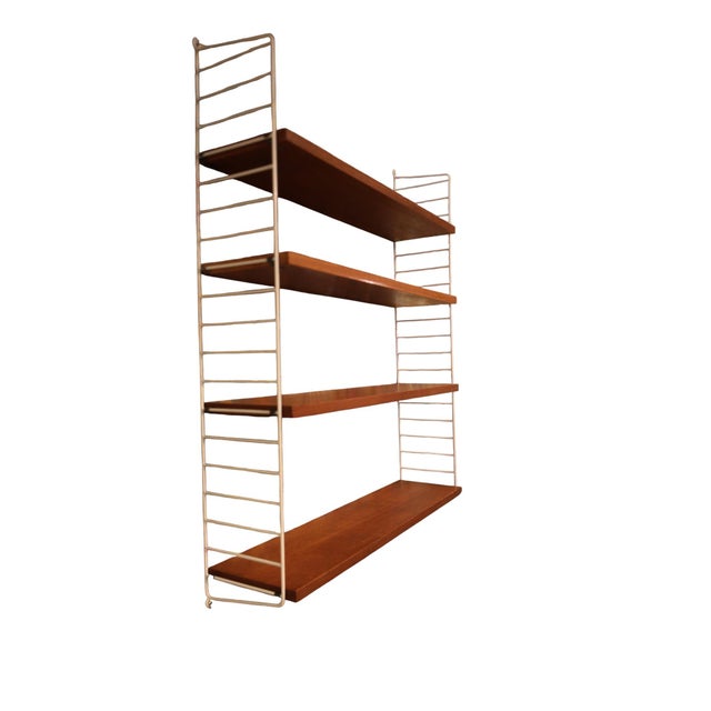 A classic original String shelf with four shelves in teak and two white wire ends. The warm, slightly darker reddish-brown...