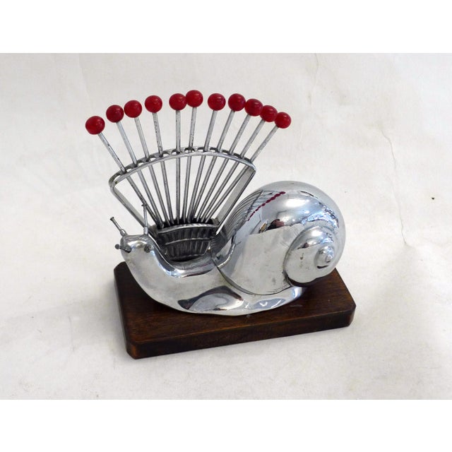 Art Deco snail/cocktail pick service; rectangular wooden base with chamfered corners, supporting a chromed metal snail...