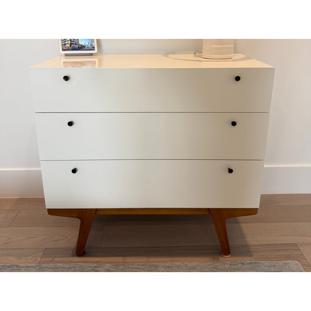 White west elm attributed mid-century modern three-drawer dresser. White lacquer body, pecan base and dark hardware....