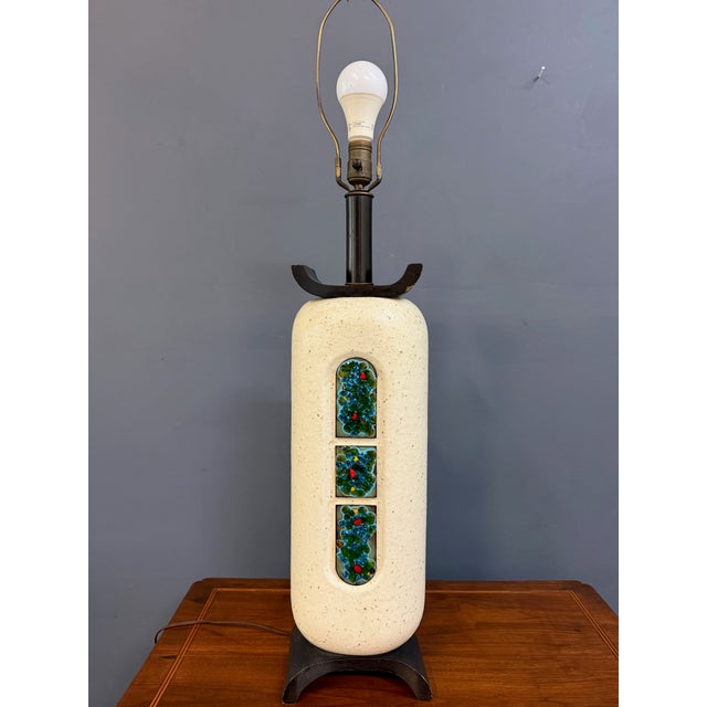 A sculptural mid-century table lamp in a tall, capsule-form ceramic body finished in a warm, pebbly cream glaze. Down the...