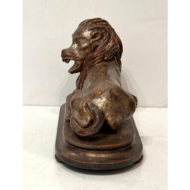 Hand-carved and silver gilded reclining lion on attached footed base.