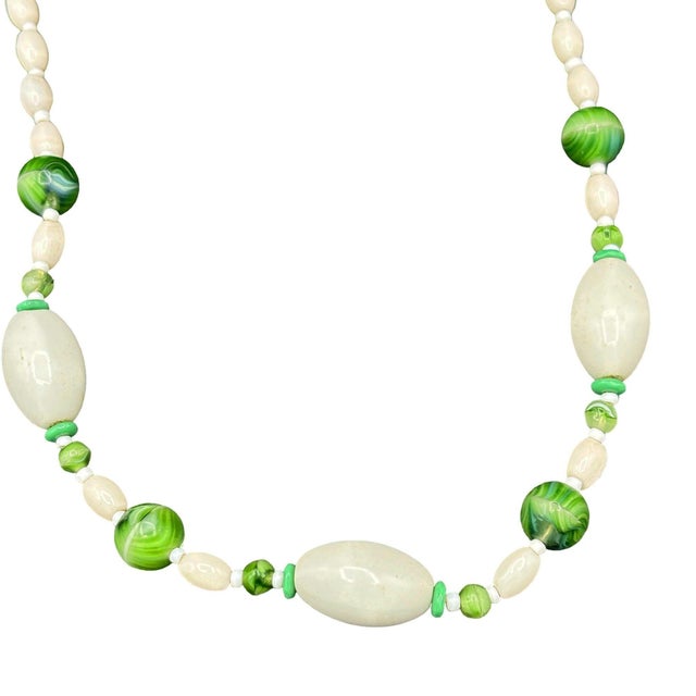 The necklace is composed of finely carved ivory-toned "ivorine" glass beads interspersed with vibrant leaf-green glass...