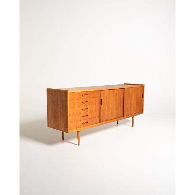 Teak sideboard with five drawers, two sliding doors, and internal compartments with shelves, featuring tapered oak legs...