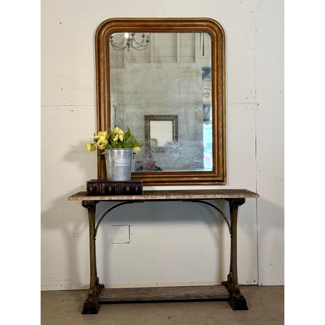 This antique French gilt mirror features a lovely aged patina, with intricate floral gilt detailing and beaded accents....