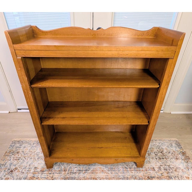 This solid maple wood bookcase, characterized by its Mid-Century/Early Colonial Revival styling, has a warm honey finish...