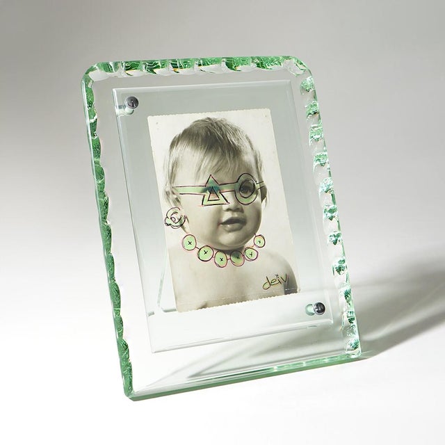 A tabletop photo frame from the 1960s, made entirely of transparent glass. Its most distinctive feature is the large outer...