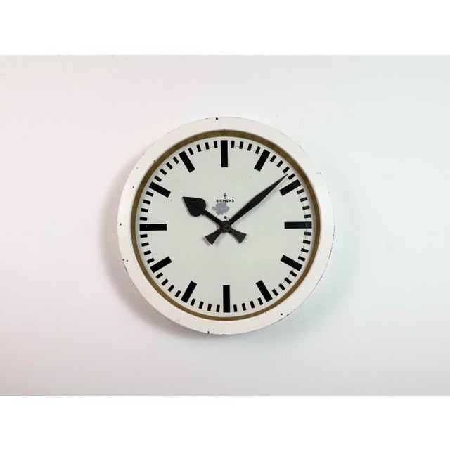 This wall clock was produced by Siemens in Germany during the 1950s. It features a white (beige) metal frame, a metal dial...