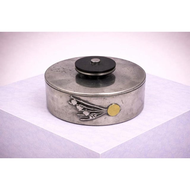 The cylindrical form features a softly patinated pewter surface, decorated with a stylized burst of playing card...