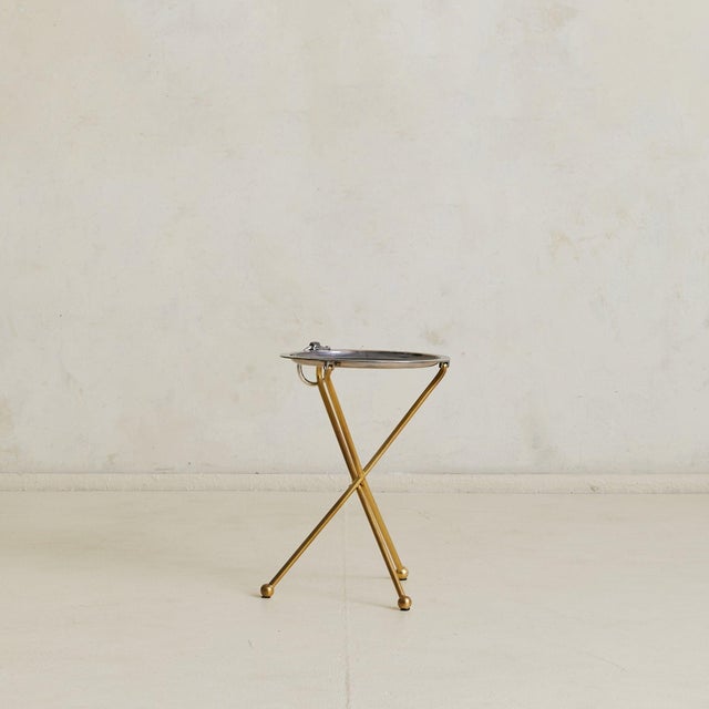 A Spanish folding tray table in brass and silverplate, circa 1960s. The circular top rests on a patinated brass tripod...
