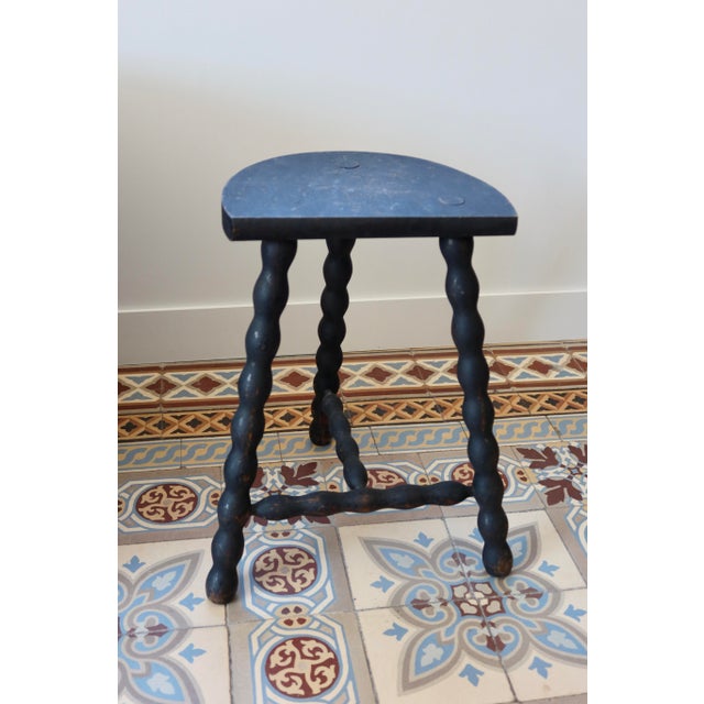 Antique tripod stool in turned wood, with a crescent-shaped seat and a beautiful worn black patina that reveals the wood...