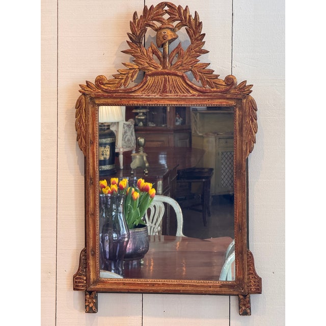 Elegant 19th-century giltwood mirror with intricate hand-carved detailing. The crest features a laurel wreath encircling a...
