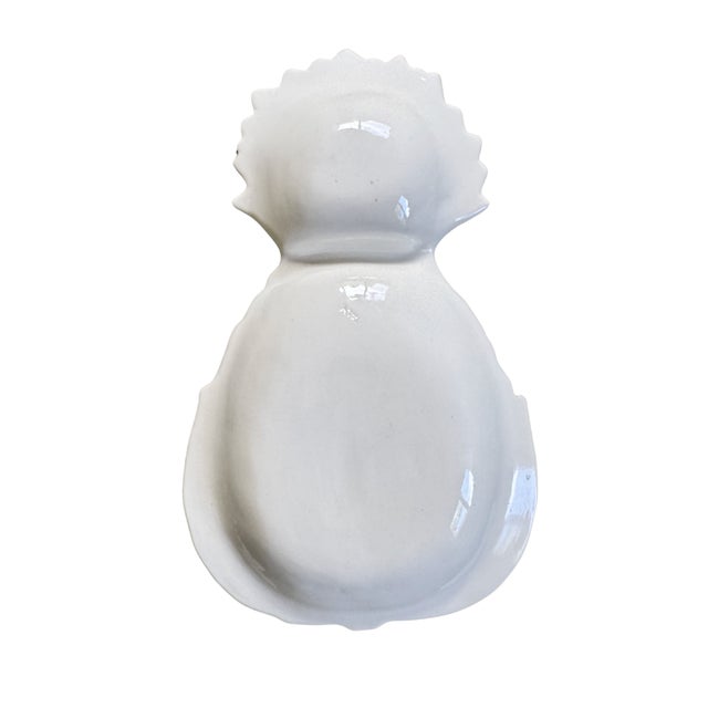 A pristine white-glazed ceramic appetizer dish in the form of a sculpted pineapple, with delicate chartreuse leaf...