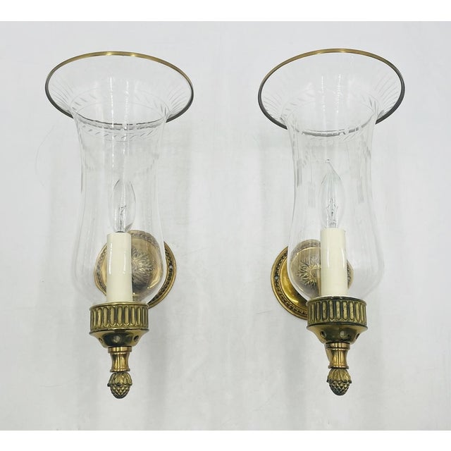 A handsome pair of English brass hurricane wall sconces by Charles Edwards of London, masterfully crafted in England and...