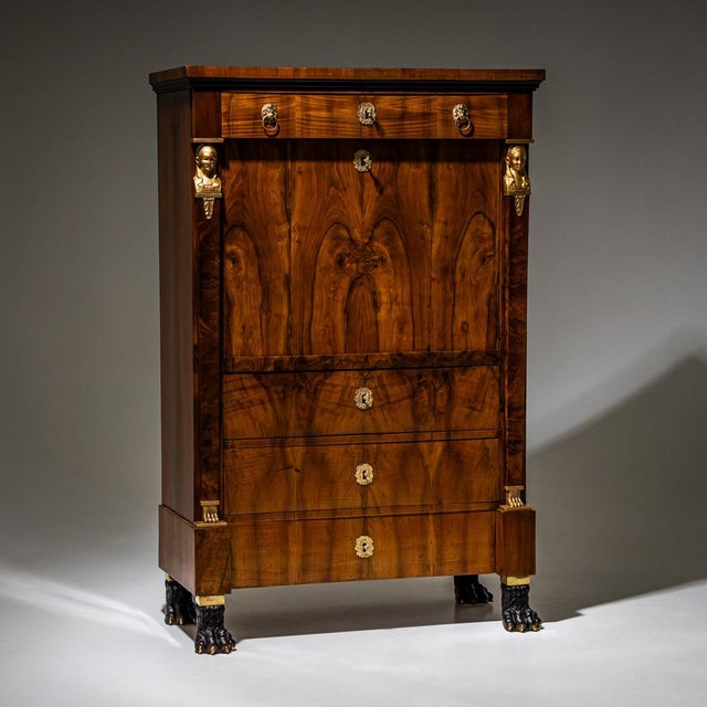 Empire secretary featuring four drawers and a flat fall-front writing surface. The piece stands on ebonized and gold-...