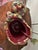 The base of the tureen is a deep crimson red sleigh. It is heavily decorated with ornate, swirling rococo-style scrolls,...