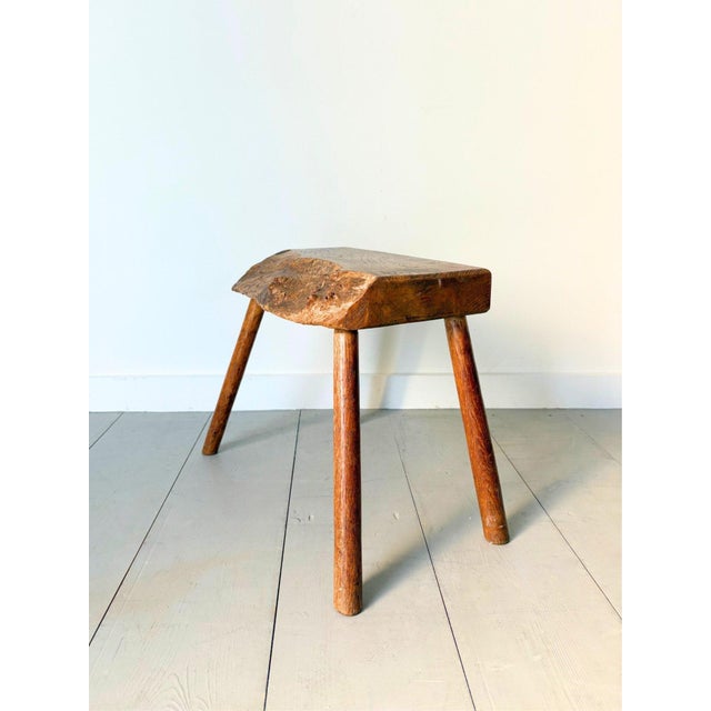A primitive side table stool with a simple honest construction with splayed legs and an organic slab top retaining its...