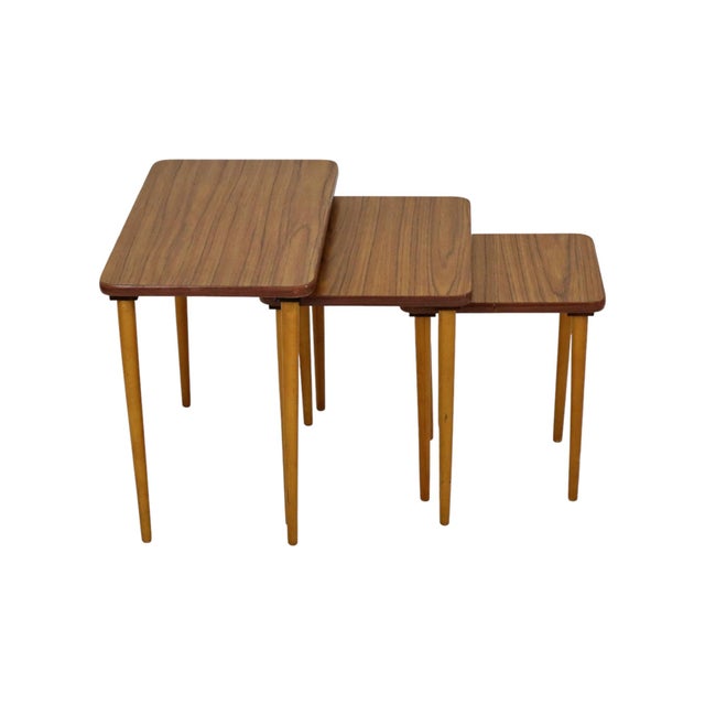 A beautiful set of three nesting tables featuring walnut-patterned formica tops and solid beechwood tapered legs—a vintage...