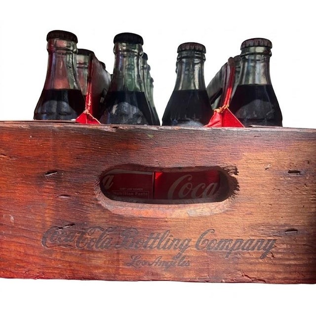 A charming Coca-Cola display set featuring a vintage wooden Coca-Cola crate paired with assorted Coca-Cola glass bottles...