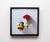 This artwork features a whimsical juxtaposition of a ceramic bee and a vibrant red carnation, both meticulously rendered...