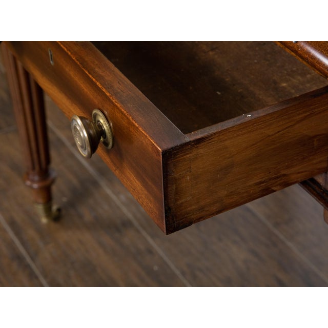 An English mahogany writing table from the 19th century, with green leather top, gilt accents, carved reeded legs, two...