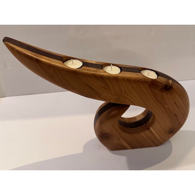 A sculptural three-candle holder, hand carved from two contrasting woods, a lighter honey-toned wood makes up the main...