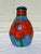 A funky coil pot painted with vibrant colors- orange, blue and green. The pot has bright large poppies around the middle...