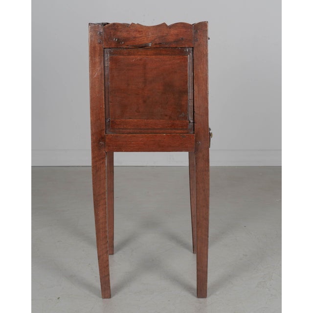 A 19th century Country French side table or nightstand made of solid walnut, with raised panels, open niche and a small...