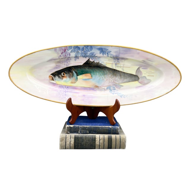 An elongated oval porcelain platter featuring a beautifully painted fish in teal, blue, and soft peach, surrounded by...