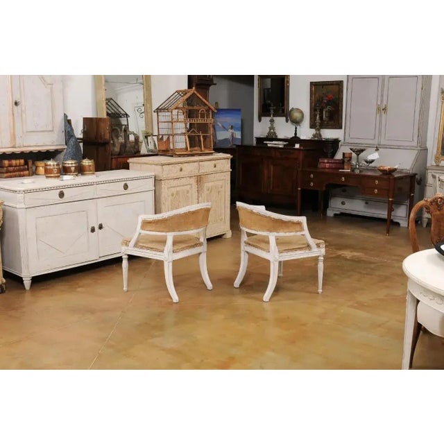 A pair of Swedish Gustavian style painted wood tub chairs from the late 19th century, with curving backs, carved campanula...