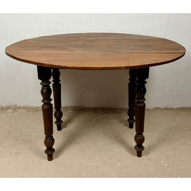 Charming Spanish drop-leaf table crafted from wood, featuring a rounded top and elegant turned legs. The hinged leaves can...
