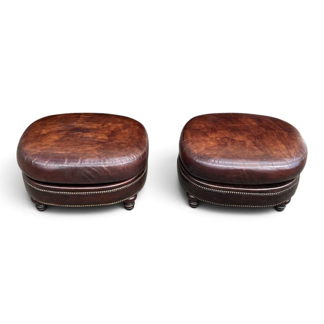 This pair of vintage oval leather ottomans brings warmth and classic character to a living room, library, or study. Rich...