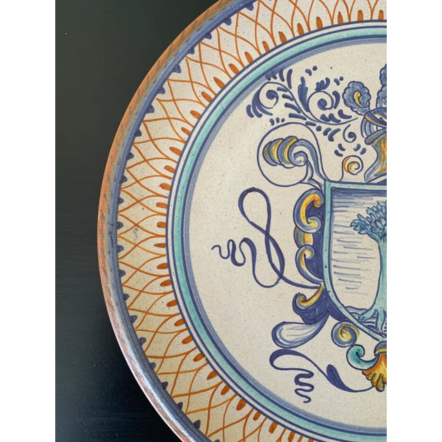 A beautiful hand painted blue, cream, and yellow faience pottery wall plate featuring a coat of arms crest. By Fidia...