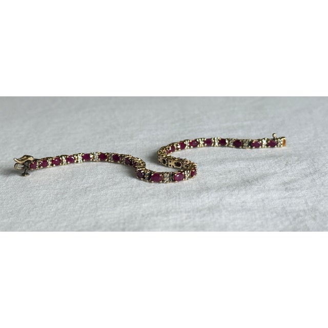 A classic vintage 14K yellow gold tennis bracelet featuring twenty-seven oval-cut natural rubies alternating with pairs of...