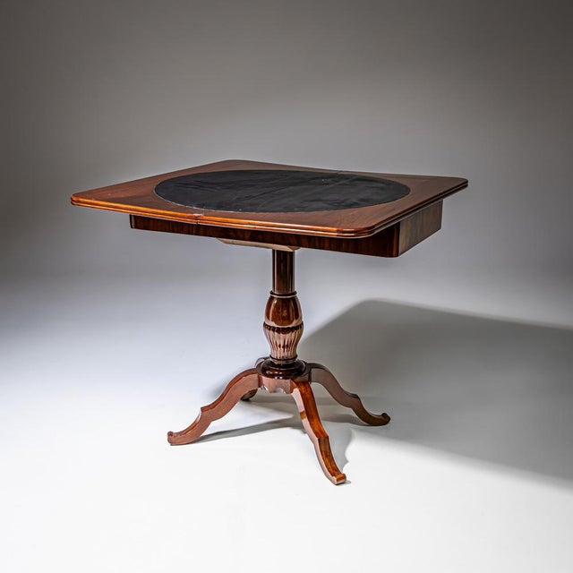 This table stands on four waved feet above a fluted shaft that supports the square folding table top. The open top is...
