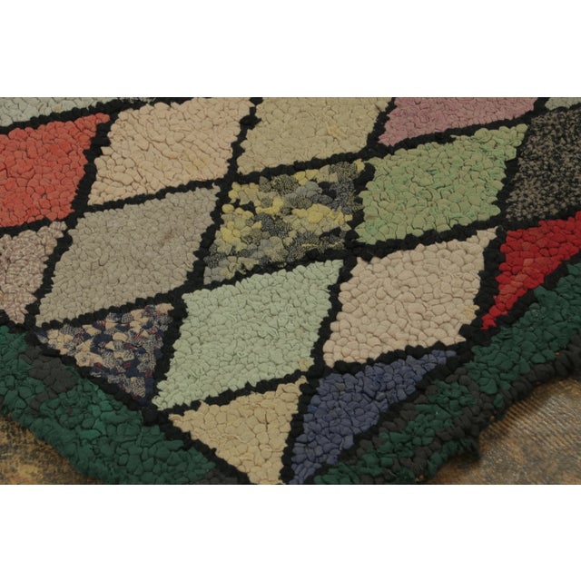 This antique 2x4 hooked rug, circa 1920–1929, features a lively harlequin diamond pattern rendered in soft pastels and...