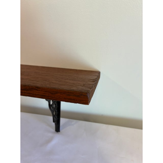 Vintage wood wall shelf with decorative cast iron brackets. This piece features a solid wood top with ornate black metal...