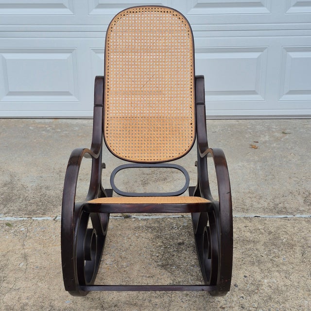 This is a vintage Thonet style bentwood rocking chair with a dark stained steam bent wood frame and natural cane back and...