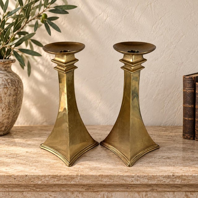 A striking pair of vintage brass candlesticks with bold architectural lines and dramatic four-point geometric bases. Made...