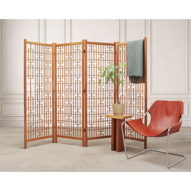 An impressive mid-century modern four-panel teak geometric latticed folding screen or room divider in light honey-toned...