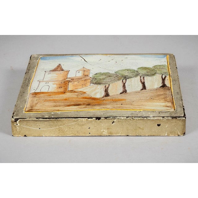 An 18th-century Talavera lead tile, square in form, decorated with a tin-glazed naïve depiction of a simple castle motif...