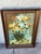 This is a framed floral still-life painting. Artwork • Depicts a loose bouquet of yellow and orange flowers arranged in a...