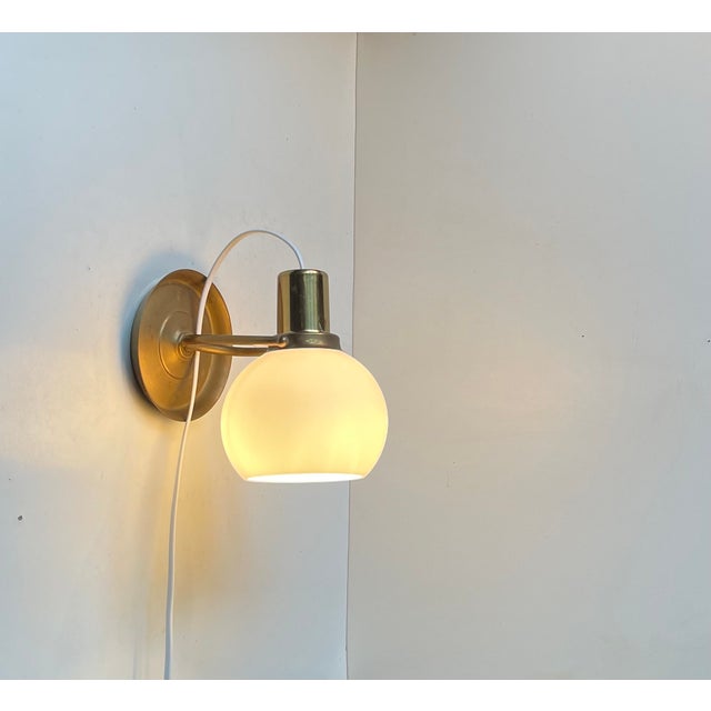 An elegantly crafted wall sconce in patinated brass featuring a frosted spherical opaline glass shade. Unknow Scandinavian...